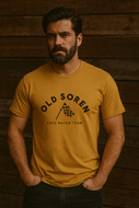 Man wearing a mustard yellow t-shirt with 'Old Soren Cafe Racer Team' text against a wooden background