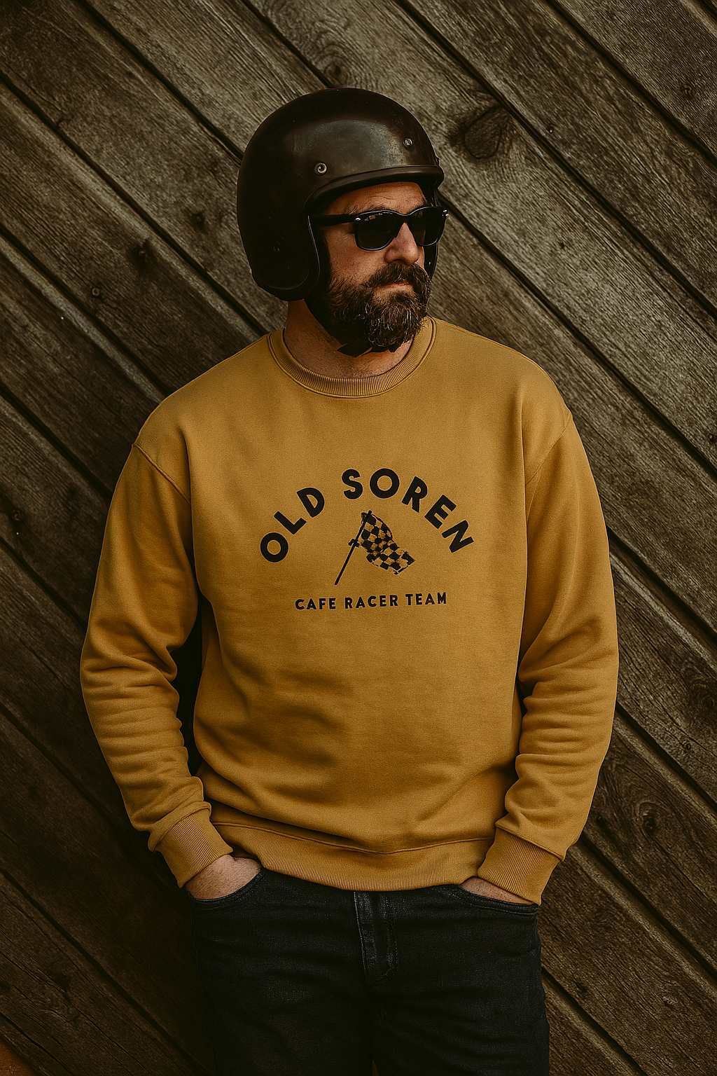 Man wearing a mustard yellow sweatshirt with 'Old Soren' branding against a wooden wall.
